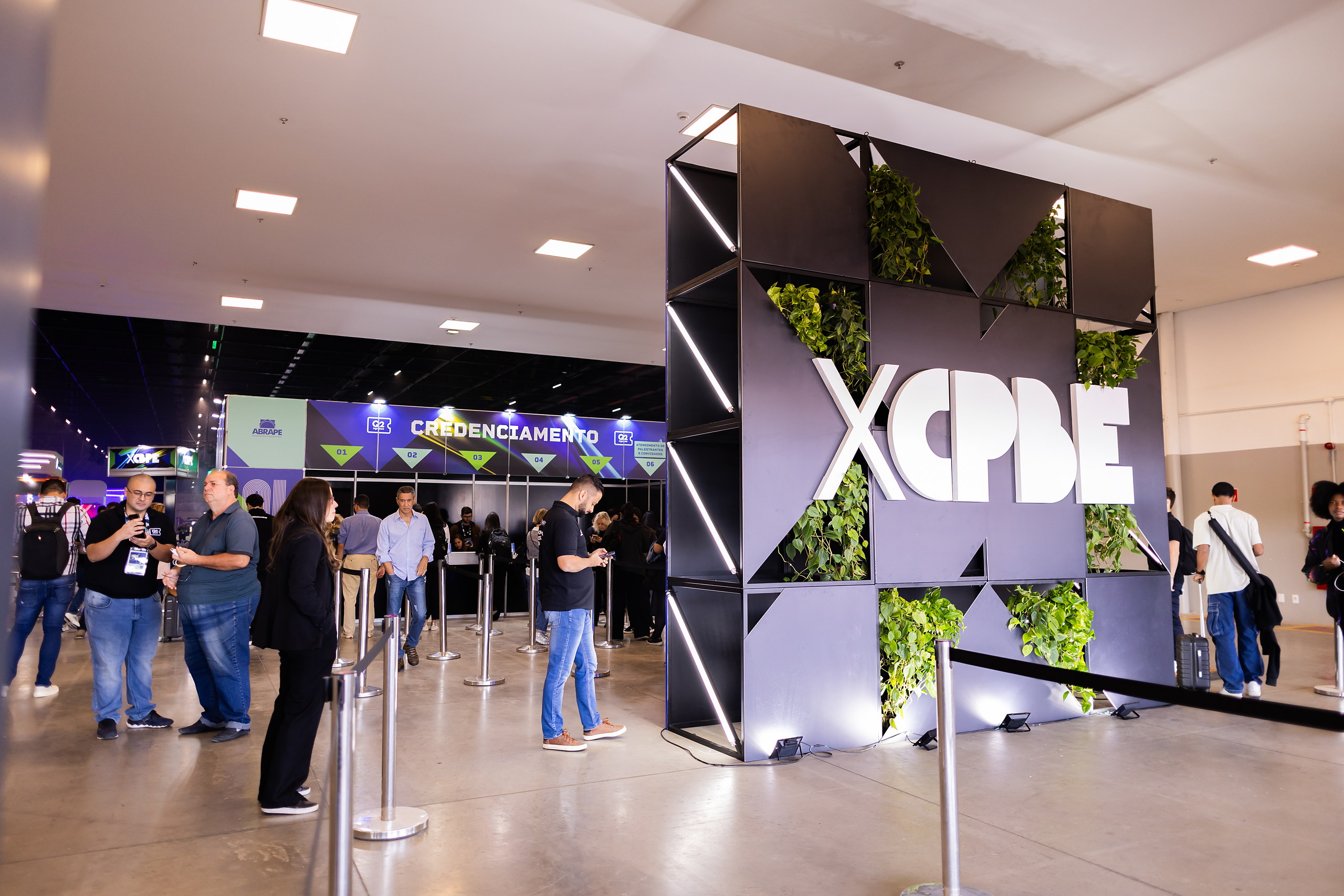 Estande do XCBPE com parede verde e visitantes ao fundo